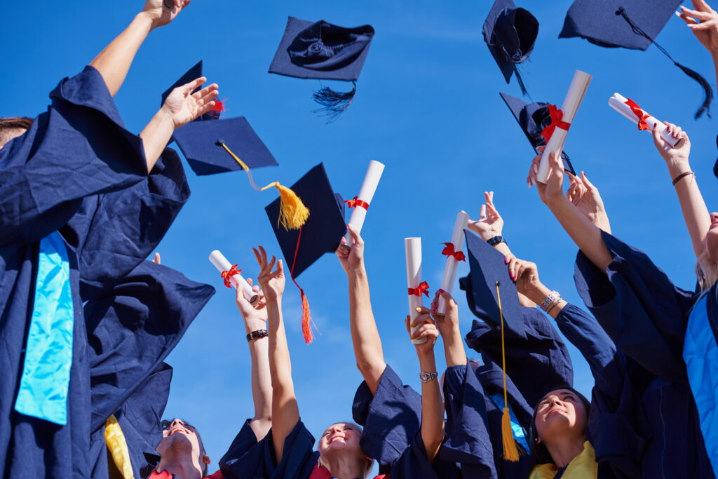 high school students graduates tossing up hats over blue sky.