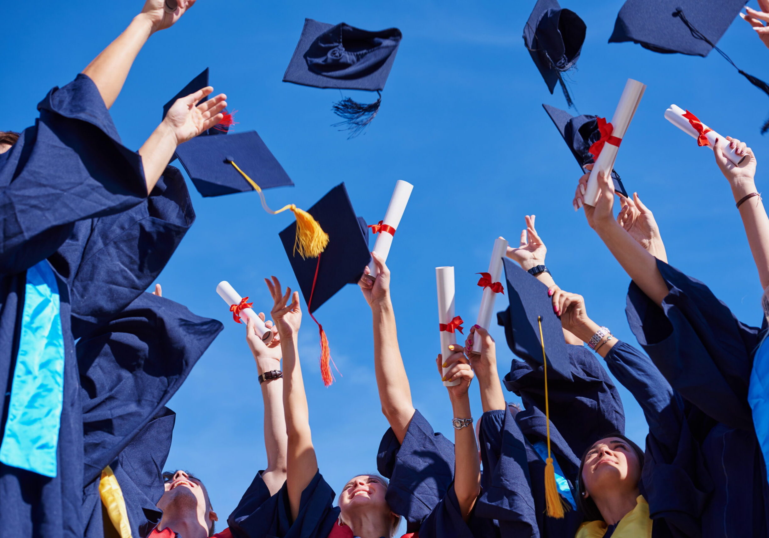 high school students graduates tossing up hats over blue sky.